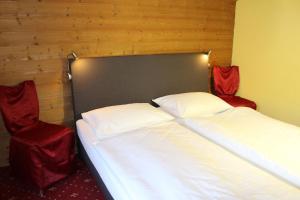 two beds in a room with two red chairs at Hotel Lindwurm in Bad Goisern