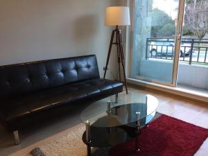 sala de estar con sofá de cuero negro y mesa de cristal en Apart Hotel R&P Depto A, en Puerto Varas
