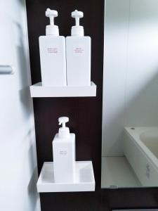Zwei weiße Flaschen mit Duftstoffen befinden sich auf Regalen im Bad. in der Unterkunft Kashiwa House Furano in Furano