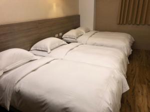 three beds in a room with white sheets and pillows at The Riverside Hotel Hengchun in Hengchun