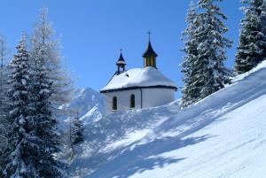 kościół na śnieżnym wzgórzu z pokrytymi śniegiem drzewami w obiekcie Apart Oberhaus w mieście Kappl