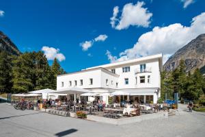 ein weißes Gebäude mit Tischen und weißen Sonnenschirmen in der Unterkunft Gletscher-Hotel Morteratsch in Pontresina