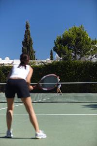 a woman swinging a tennis racket on a tennis court at NAU Sao Rafael Suites - All Inclusive in Albufeira
