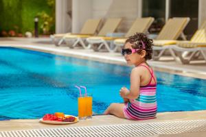 a little girl sitting next to a swimming pool with a plate of fruit at Golden Orange Hotel in Antalya
