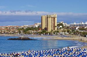 a beach with blue and white umbrellas and people on the beach at Torres del Sol in Playa de las Americas