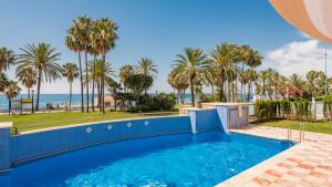 a pool with palm trees and the ocean in the background at Apartamento Noray Playa in Marbella