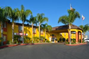 a yellow hotel with palm trees in front of it at Americas Best Value Inn & Suites Madera in Madera