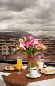una mesa con un jarrón de flores y platos de comida en Hotel Mabey Cusco, en Cusco