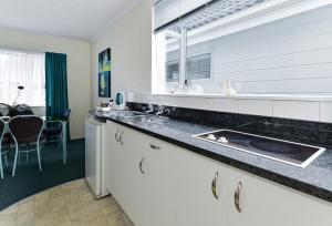 a kitchen with white cabinets and a sink and a window at Palm Court Motor Inn in Rotorua