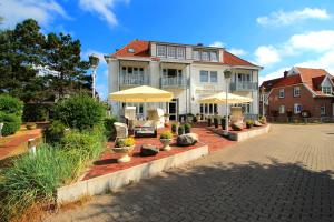 une grande maison blanche avec des parasols en face de celle-ci dans l'établissement Hotel De Insulåner, à Langeoog