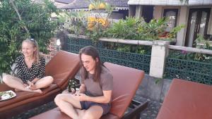 two women sitting on a chair looking at their cell phones at Solaluna Beach Homestay in Amed