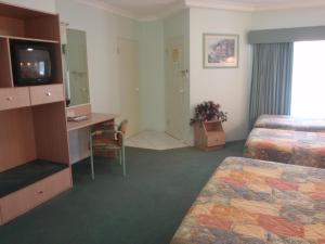a hotel room with a bed, television and a desk at Runaway Bay Motor Inn in Gold Coast