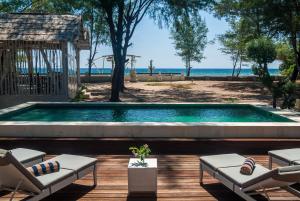 a swimming pool with chairs and a view of the ocean at Coral Flora Villa Beach Front in Gili Trawangan