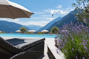 ein Pool mit einem Sofa, einem Sonnenschirm und Blumen in der Unterkunft Hotel Panorama in Schenna