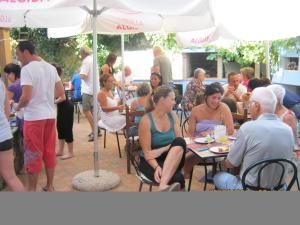 Su Cantaru Guesthouse في Villanova Monteleone: مجموعة من الناس يجلسون على الطاولات تحت مظلة