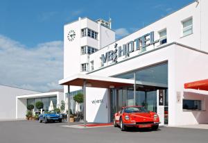 une voiture rouge garée devant un bâtiment blanc dans l'établissement V8 HOTEL Classic Motorworld Region Stuttgart, à Böblingen