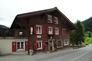 a wooden house with red shutters on a street at Berggasthaus Gemsli in Sankt Antönien