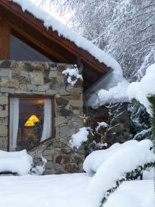 una casa de piedra en la nieve con una lámpara en la ventana en Hostería Brisas del Cerro en Villa La Angostura