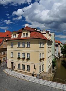 a yellow building with a red roof next to a river at Hotel Certovka in Prague