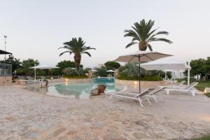 een zwembad met stoelen, parasols en palmbomen bij Masseria Valente in Ostuni