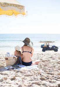 a woman sitting on a beach with a surfboard at Tingirana Noosa in Noosa Heads