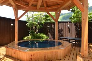 a hot tub on a deck with a wooden pergola at Schole Hakuba in Hakuba