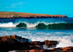 a large wave in the ocean with a house in the background at Castletown Hotel in Castletown