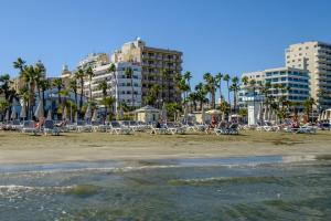 einen Strand mit Liegestühlen, Palmen und Gebäuden in der Unterkunft Les Palmiers Beach Boutique Hotel & Luxury Apartments in Larnaka