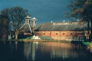 an old barn with a black roof next to a body of water at Causeway Lodge in Bushmills