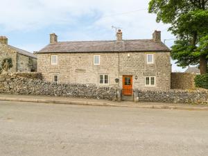 a stone house with a stone wall and a red door at Box Tree Cottage in Buxton