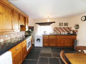 uma cozinha com armários de madeira e uma máquina de lavar louça branca em Rose Cottage em lower hawthwaite