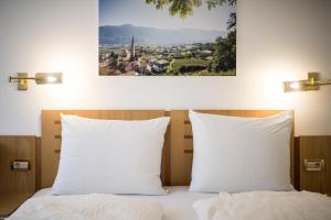 uma cama com almofadas brancas e uma fotografia na parede em Mondschein Rooms em Lana