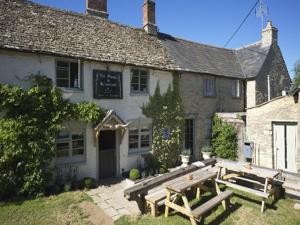 um edifício com dois bancos de madeira à sua frente em The Plough Inn em Little Faringdon