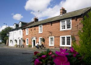 duas pessoas sentadas num banco do lado de fora de um edifício de tijolos em The Kings Arms Temple Sowerby em Temple Sowerby