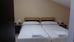 um quarto com 2 camas com lençóis brancos e almofadas em Pensión El Tabanu em Celorio
