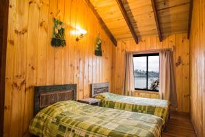 two beds in a wooden room with a window at Apart hotel Puchaley Lafquen in Panguipulli