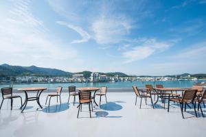een groep tafels en stoelen op een patio met uitzicht op het water bij Fortuna Hotel in Tongyeong