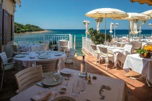 a restaurant with white tables and chairs and the ocean at Hotel Le Maquis in Porticcio