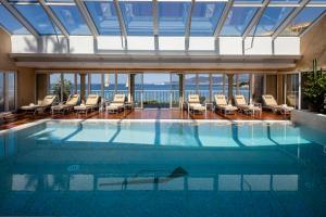 a swimming pool with chairs and the ocean in the background at Hotel Le Maquis in Porticcio