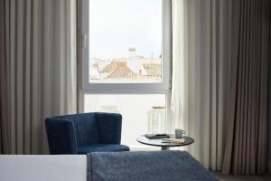 a room with a blue chair and a table and a window at Occidental Faro in Faro