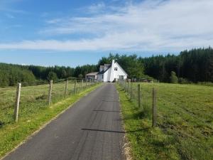 eine Straße, die zu einem weißen Haus auf einem Feld führt in der Unterkunft An Cois Na H-Aibhne in Skeabost