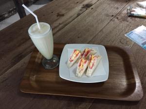 a plate of sandwiches and a drink on a tray at Lia Jaya Bungalows in Gili Meno