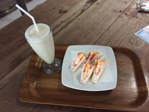 a tray with a plate of sandwiches and a drink at Lia Jaya Bungalows in Gili Meno