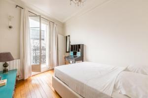 a white bedroom with a bed and a window at Veeve - Cosy Gambetta in Paris