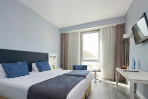 a hotel room with a bed and a desk and a television at Occidental Faro in Faro