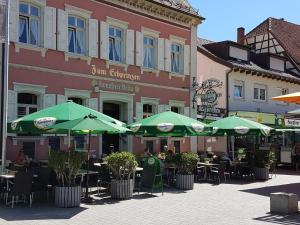 Hotel Restaurant Erbprinz Walldorf في فالدورف: مجموعة طاولات بمظلات خضراء امام المبنى