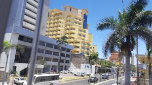 a yellow building on a city street with palm trees at Condominio Ibis Mazatlán in Mazatlán