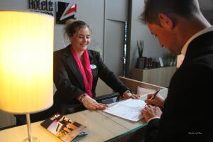 a man and a woman signing a document at a desk at Hotel de la Source in Francorchamps