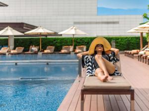 una mujer con sombrero sentada en una silla junto a una piscina en Pullman Bangkok King Power en Bangkok