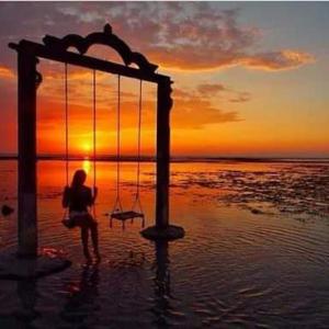 a person sitting on a swing in the water at sunset at Cape Rose in Gili Trawangan